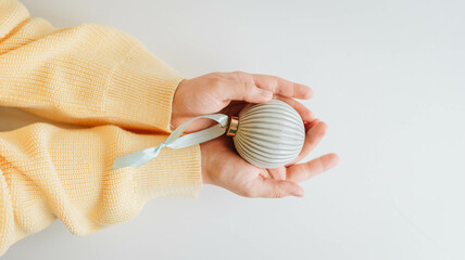 A woman in a yellow sweater holds a blue Christmas ball in her hands. Christmas concept in Ukrainian colors.
