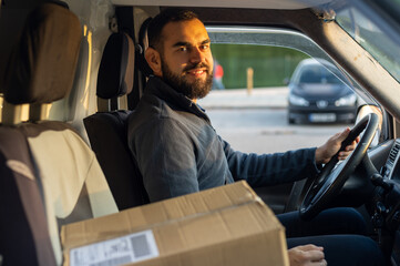 Delivery man working inside a van next to a parcel ready to drive. Looking at camera
