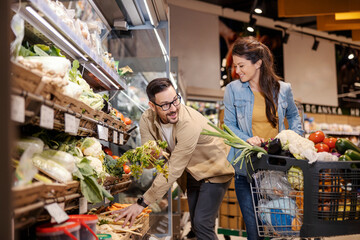 Happy couple is purchasing vegetables in supermarket.