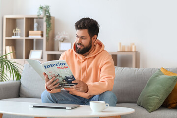 Handsome bearded man reading magazine on grey sofa at home