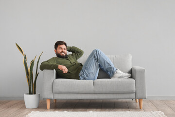 Handsome bearded man lying on grey sofa near light wall