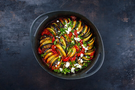 Modern style traditional Greek briam with sliced vegetable, potatoes and feta cheese served as top view in a design cast-iron pot with copy space