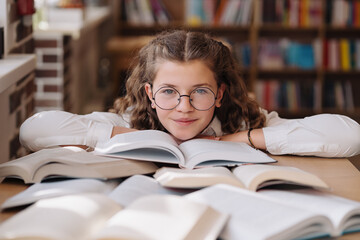 Attractive happy young girl student studying at the college library, sitting at the desk