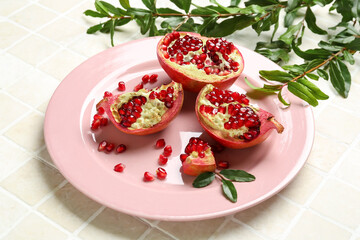 Plate with fresh pomegranates and plant branches on light tile, closeup