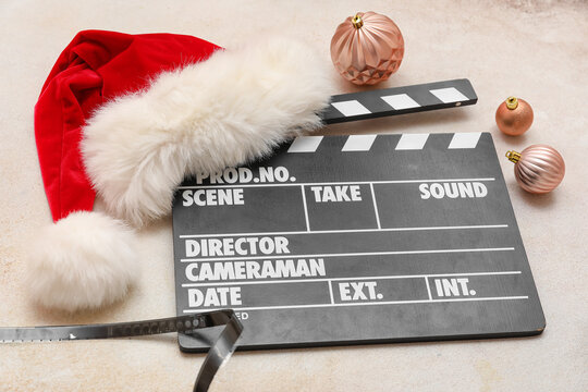 Movie clapper with Santa hat, Christmas balls and film reel on light background