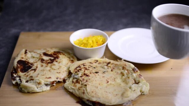 Video of a hand taking a cup of hot chocolate served with 2 pupusas and curtido. National Salvadoran national dish.