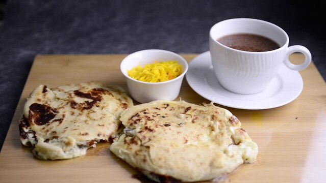 Video of hand picking a pupusa served with acompanying pupusa, curtido and hot chocolaate. Traditional national dish from El Salvador.