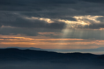 Sun rays coming down from some clouds above mountains - 546099438