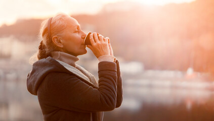 A woman, lady drinks a coffee and enjoys the sunset.