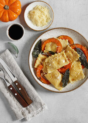 Homemade Pumpkin Ravioli with ricotta cheese served sage butter , cheese, pieces of pumpkin and cutlery on linen napkin . top vertical view