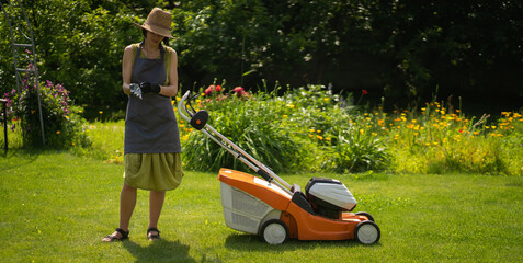 A girl is mowing a lawn in the backyard in the summer.