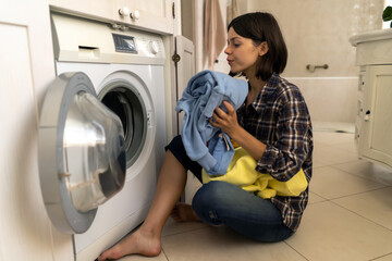 Girl puts clothes in washing mashine.