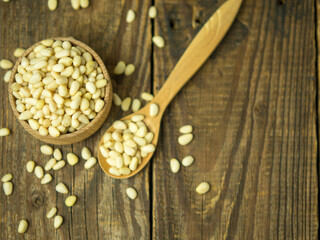 Heap of raw pine nuts in a wooden bowl and spoon. Peeled pine nuts on an old wooden table.