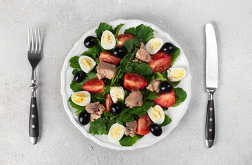 Salad with arugula, cod liver, quail eggs and cherry tomatoes on white plate on gray background, Top view