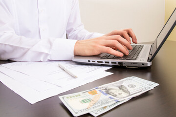 close-up of human hands typing on a computer keyboard. in the foreground are dollar bills