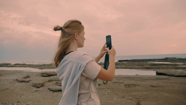 Woman tourist taking photo picture sunset sunrise beach dramatic sky use smartphone display