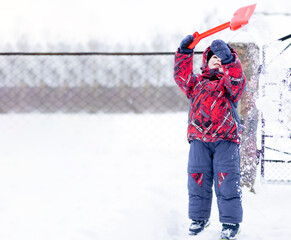 Little boy playing with a red shovel in the snow. Winter activity