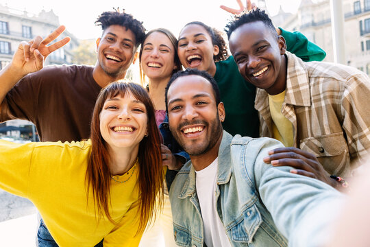Happy young group of multiracial best friends having fun together outdoors. Millennial diverse people enjoying time together taking selfie portrait in city street