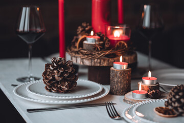 Rustic table decor for Christmas or New Year family dinner. Centrepiece with red candle, dry orange, cone, cinnamon, anise. Zero waste eco-friendly home. Cozy atmosphere, dark background. Close up