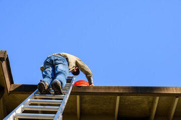 Senior man standing on an aluminum extension ladder cleaning out a roof gutter
