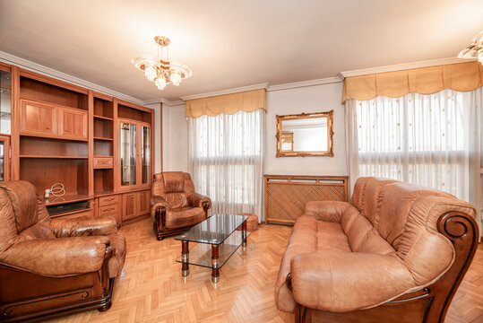 Living room of a house with oak parquet floors with wooden and brown leather tresillo and matching wooden bookcase