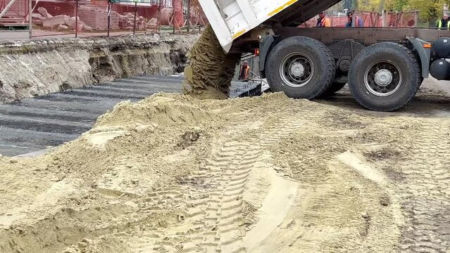 dump truck lifting a trailer and dumping sand into a trench. Unloading sand from a truck
