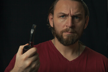 Lumberjack brutal beard muscled man in red shirt with smoking tube pipe standing on dark background