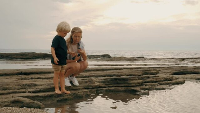 Young mother and son playing pebble at stone beach coastline sea landscape slow motion