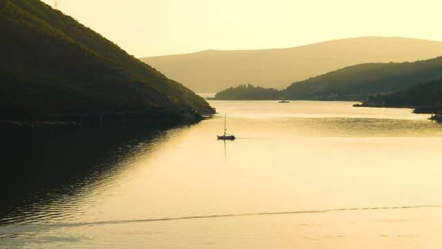 4K footage of a solo yatch boat silhouette on Kotor bay with sunset and golden color of water
