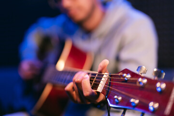 Young afro musician wearing glasses playing acoustic guitar, on dark background