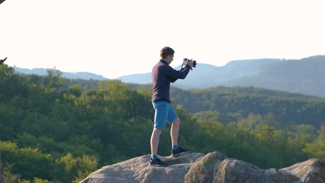 Yong man hiking in summer mountains and taking pictures of morning nature. Photographer enjoying view of beautiful landscape