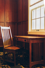 Wooden desk and chair by a bright window as sunshine beams in