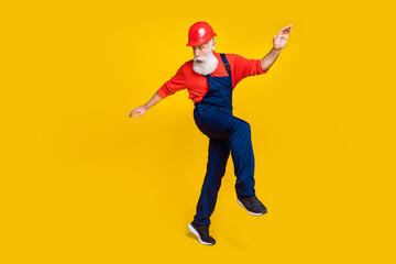 Photo of positive funky age man workwear overall red hard hat dancing having fun isolated yellow color background