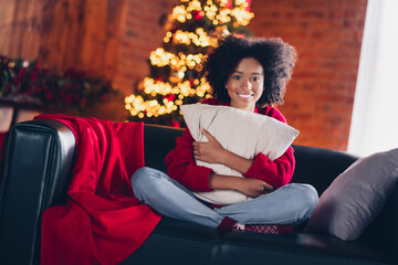 Full size photo of cheerful funny girl sitting couch hands hold cuddle cushion x-mas tree garland decor house indoors
