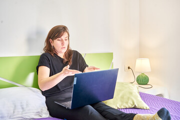 Closeup of the woman with a laptop lying on the bed chatting.