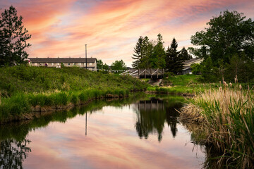 Small creek in a community recreation area with a sunset reflecting on the water at Nose Creek Park Airdrie Alberta Canada.