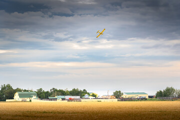 A crop duster flying over a rustic homestead after spraying a crop on the Canadian prairies in Rocky View County Alberta Canada.