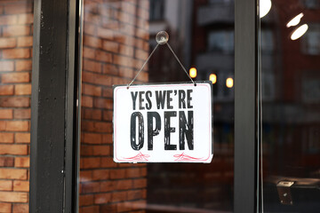 Inscription Yes we're open metal plate with black and white sign on glass door store, cafe,...