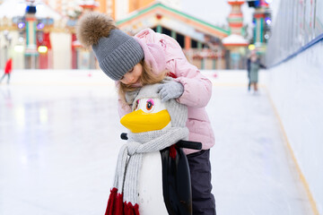 A little girl is skating on an ice rink, holding on to a support, a child is learning to skate,...
