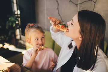 Zelfklevend Fotobehang Mother and daughter eat pizza in a cafe. © polinaloves