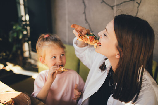 Mother and daughter eat pizza in a cafe.