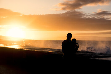 Naklejka na ściany i meble Backlight of a father and his little toddler son watching a sunset in front of the sea in Tenerife, Canary Islands