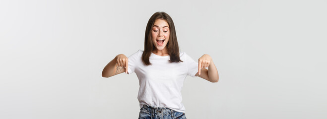 Excited happy brunette girl, looking and pointing down with amused smile