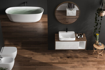 Stylish dark bathroom interior with black walls, white basin with oval mirror, bathtub, shower, plants and dark parquet floor.Minimalist cozy bathroom with modern furniture. 3D rendering