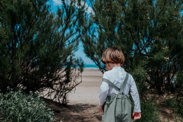 A little boy in a hat stands in a field under the sun and laughs. The boy laughs and looks away.