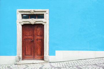 Wooden door home entrance. Italian architecture background. Vibrant color. Blue wall facade. Small town house exterior. Street of European city building.