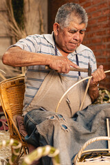 Fototapeta premium Old man using hammer for making wicker baskets at his workshop