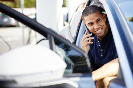 Smiling man talking on smart phone sitting in electric car