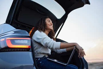 Happy woman with laptop sitting in car trunk