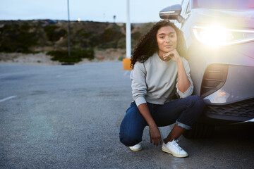 Portrait of young woman by illuminated headlight of car